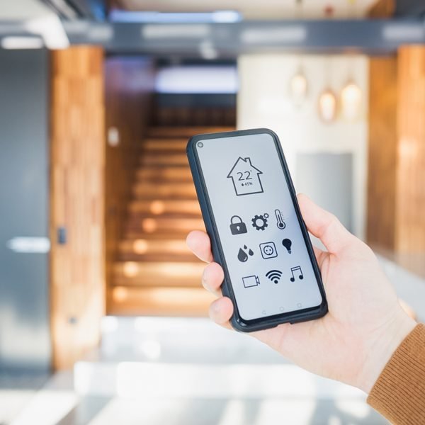 en hånd som viser frem en smarttelefon som viser oversikt over temperaturen i huset foran en trapp inne i huset.